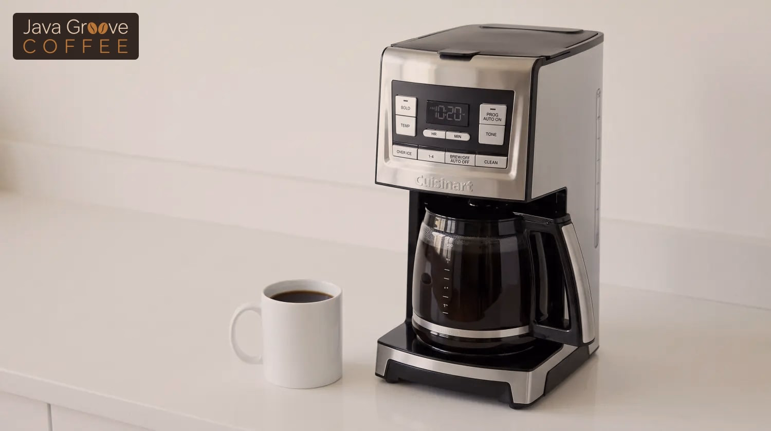 Cuisinart CBC-8500PC coffee maker with a full glass carafe beside a white mug of black coffee on a white counter